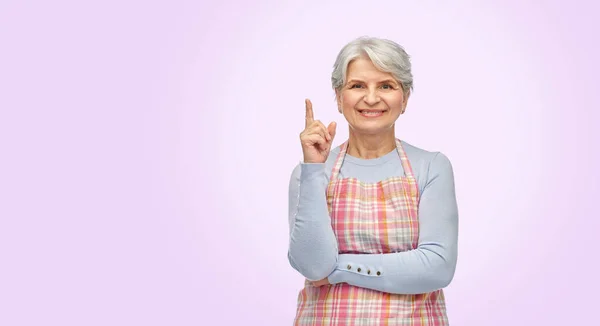 Sorrindo mulher idosa no avental apontando dedo para cima — Fotografia de Stock