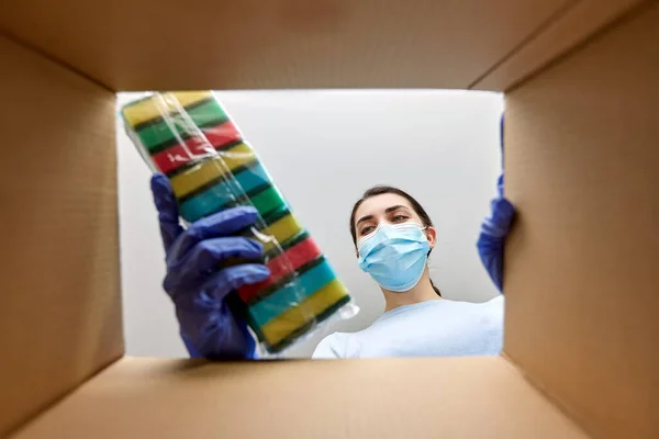 Kvinna i mask tar rengöringsmedel från lådan — Stockfoto