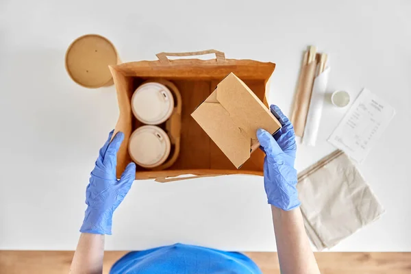 Delivery woman in gloves packing food and drinks — Stock Photo, Image