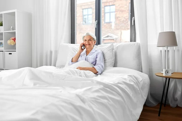 Mulher sênior chamando no smartphone na cama em casa — Fotografia de Stock