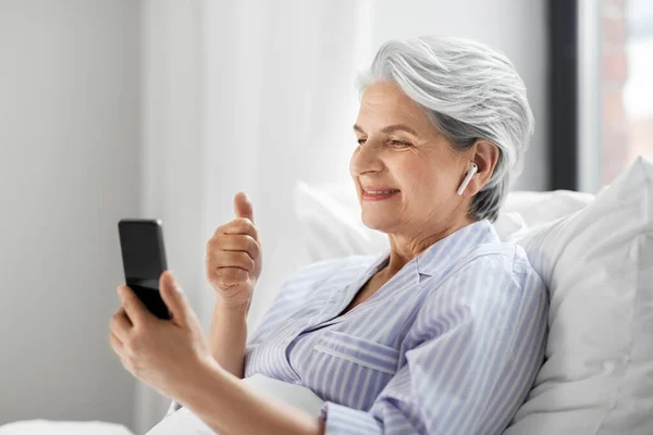Donna anziana con telefono avendo videochiamata a letto — Foto Stock