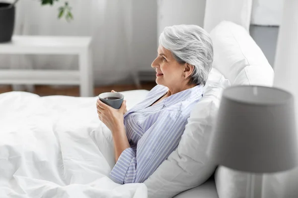 Стара жінка з чашкою кави в ліжку вдома — стокове фото