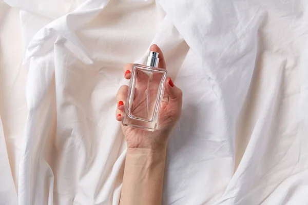 Női kéz egy üveg parfümmel fehér lapon — Stock Fotó