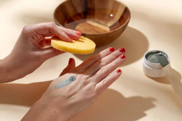 hands applying blue cosmetic clay mask to skin