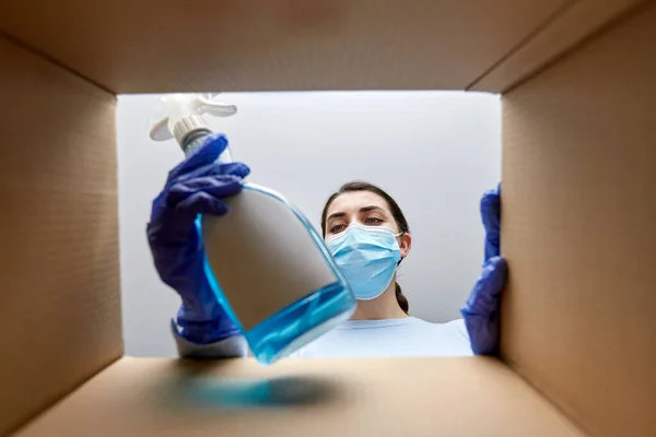 Mulher em máscara levando suprimentos de limpeza da caixa — Fotografia de Stock