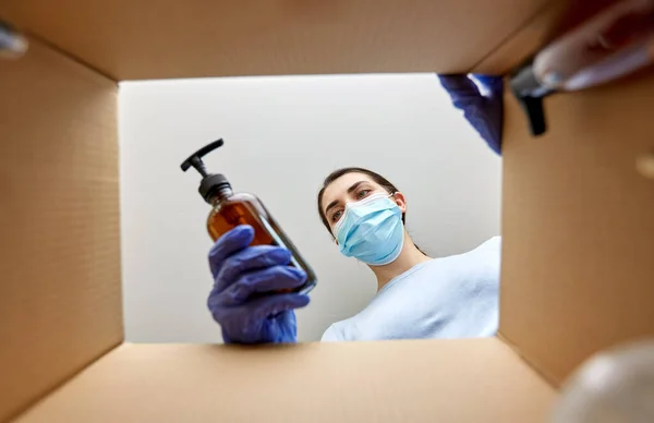 Woman in mask unpacking parcel box with cosmetics — Stock Photo, Image