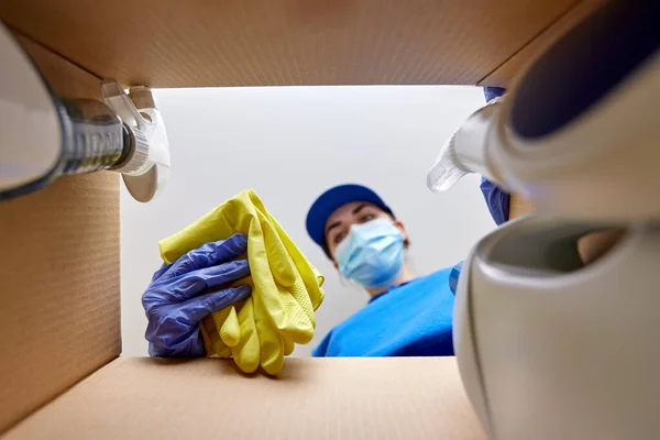 Vrouw in masker verpakking schoonmaakmiddelen in doos — Stockfoto