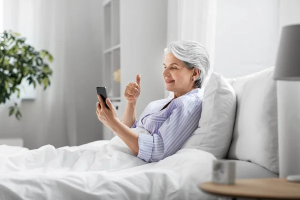 Mulher sênior com telefone ter chamada de vídeo na cama — Fotografia de Stock