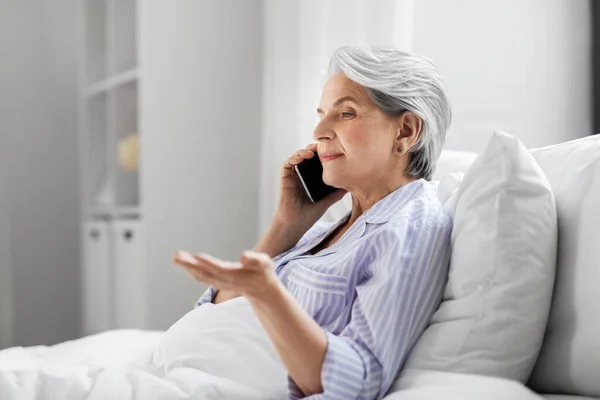 Donna anziana che chiama su smartphone a letto a casa — Foto Stock