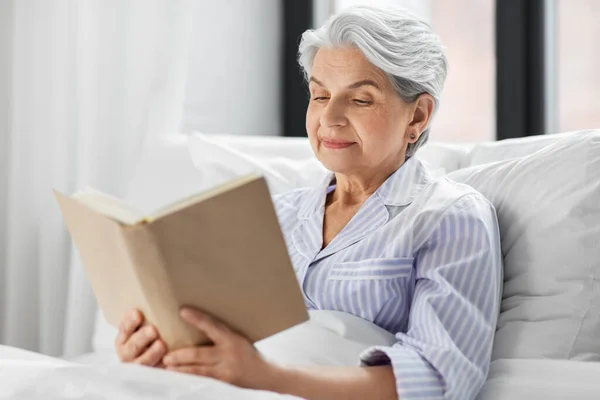 Senior femme lecture livre dans lit à la maison chambre — Photo