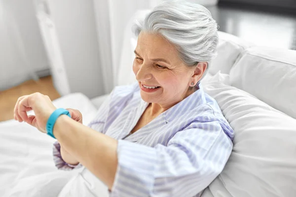 Gelukkig oud vrouw met gezondheid tracker zitten in bed — Stockfoto