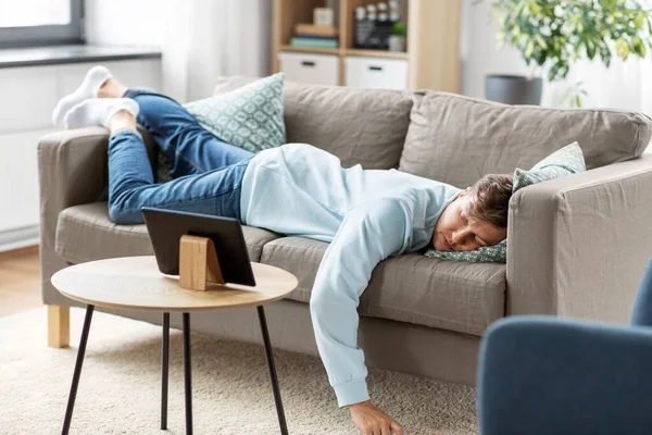 Hombre aburrido con la tableta PC acostado en el sofá en casa — Foto de Stock