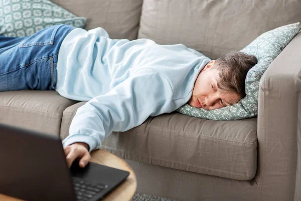 Homem entediado com laptop deitado no sofá em casa — Fotografia de Stock