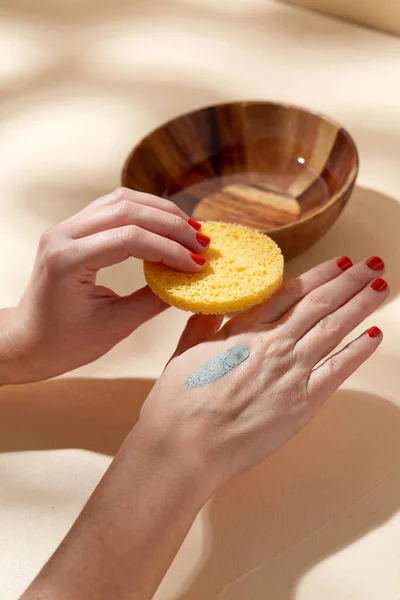 hands applying blue cosmetic clay mask to skin