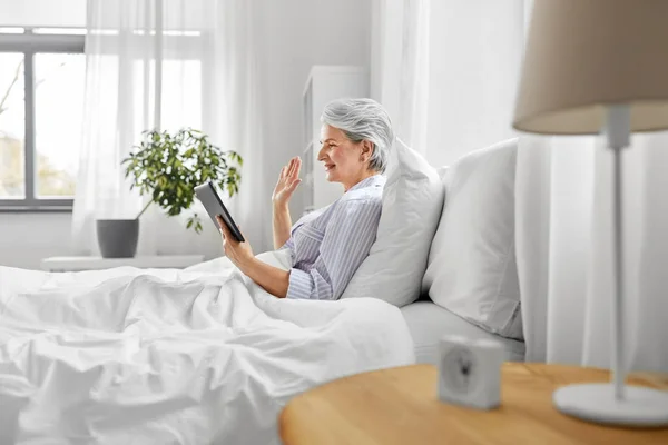 Mulher velha com tablet pc ter chamada de vídeo na cama — Fotografia de Stock