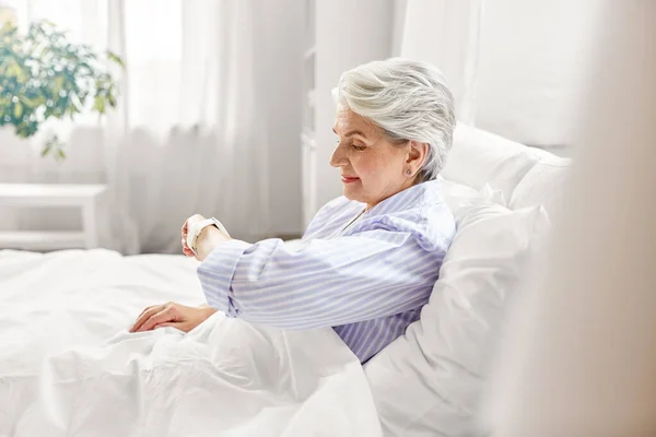 Счастливая пожилая женщина, сидящая в постели в домашней спальне — стоковое фото