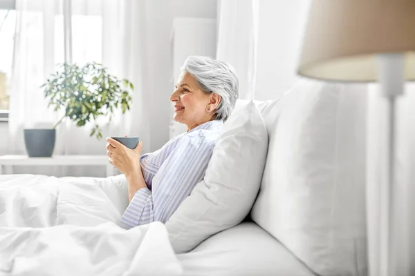 Oude vrouw met kopje koffie in bed thuis Rechtenvrije Stockafbeeldingen