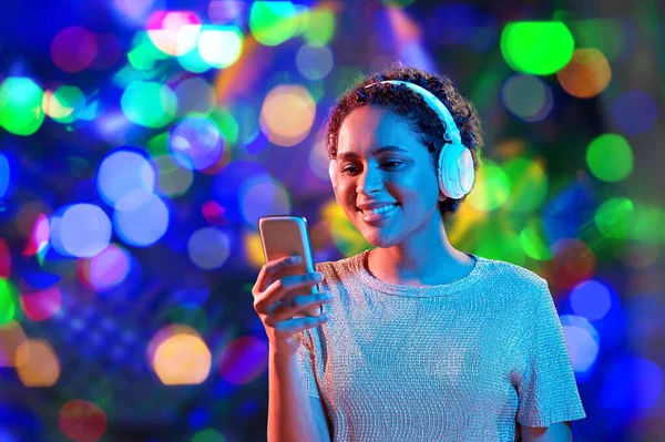 Vrouw in hoofdtelefoon met smartphone in neon verlichting — Stockfoto
