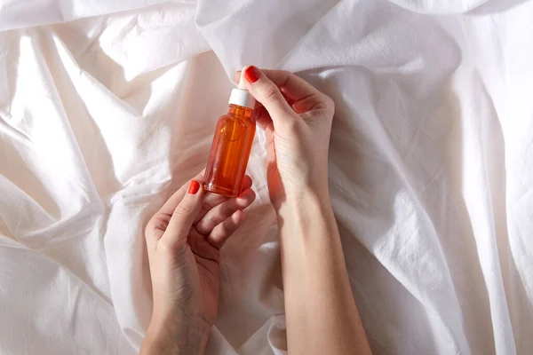 Female hands with bottle of serum on white sheet — Stock Photo, Image