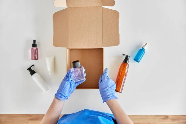 Händer i handskar förpackning paket låda med kosmetika — Stockfoto