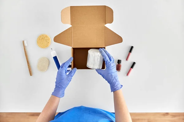 Hands in gloves packing parcel box with cosmetics — Stock Photo, Image