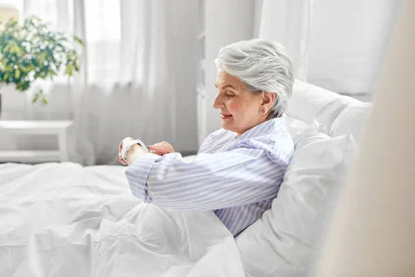 Šťastná starší žena sedí v posteli v domácí ložnici — Stock fotografie