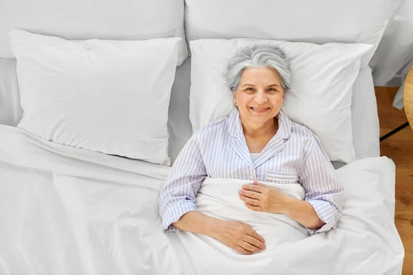 Sorridente donna anziana sdraiata a letto a casa camera da letto — Foto Stock