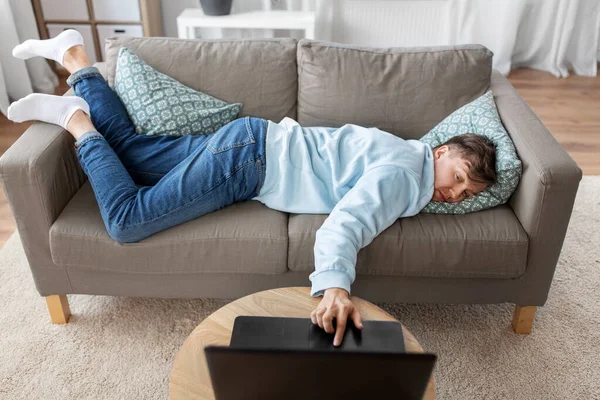Избитый мужчина с ноутбуком лежит дома на диване — стоковое фото