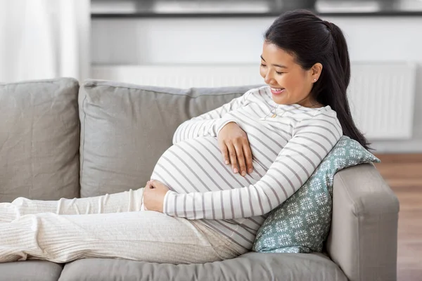 Boldog terhes ázsiai nő ül kanapén otthon — Stock Fotó
