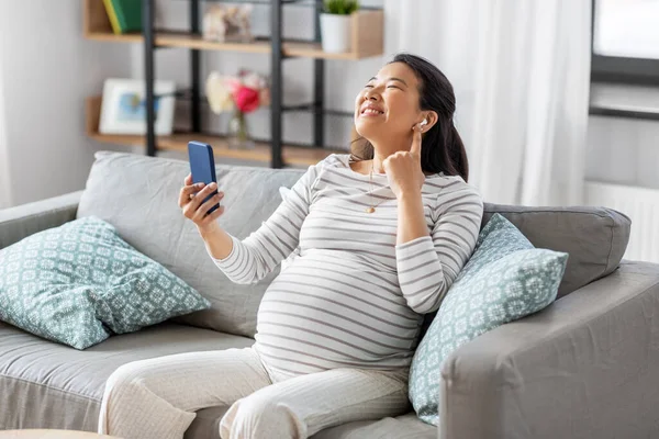 Femme enceinte avec téléphone et écouteurs à la maison — Photo