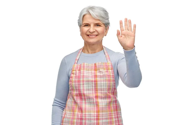 Улыбающаяся пожилая женщина в фартуке, машущая рукой — стоковое фото