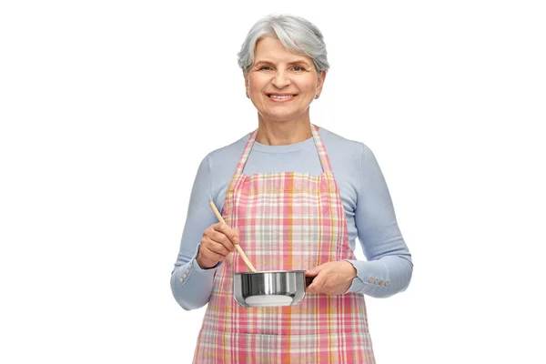 Mulher idosa em avental com panela cozinhar alimentos — Fotografia de Stock