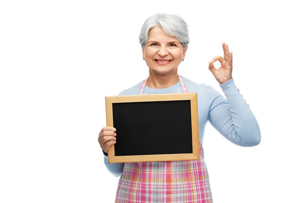 Seniorin in Schürze mit Kreidetafel zeigt ok — Stockfoto