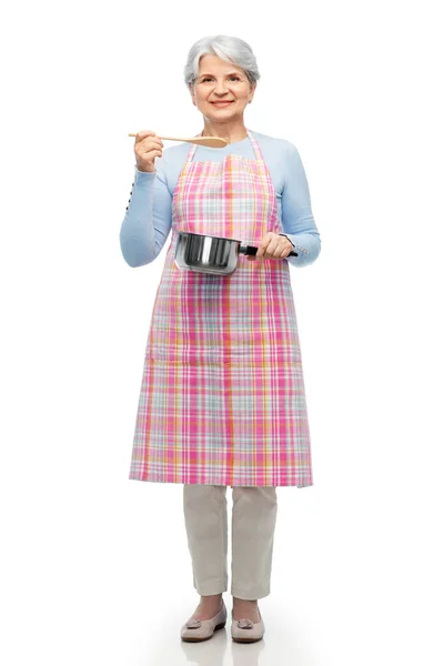 Mulher idosa em avental com panela cozinhar alimentos — Fotografia de Stock