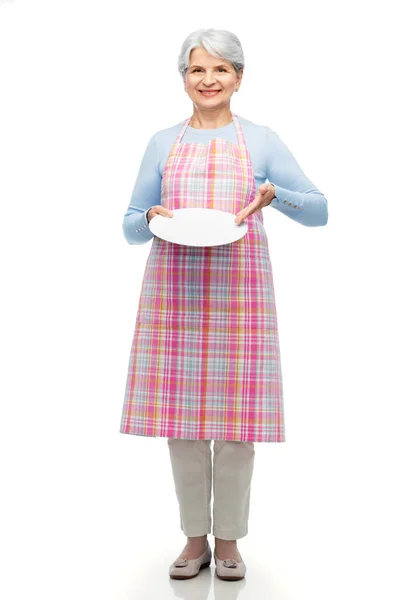 Smiling senior woman in apron with empty plate — Stock Photo, Image