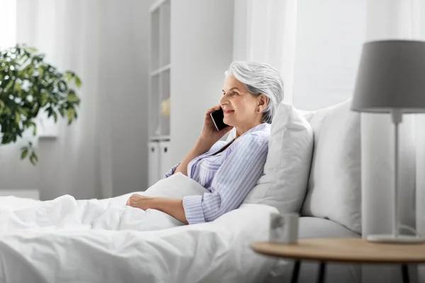 Пожилая женщина звонит на смартфон в постели дома — стоковое фото