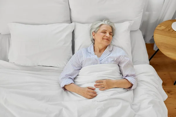 Счастливая пожилая женщина спит в постели в домашней спальне — стоковое фото