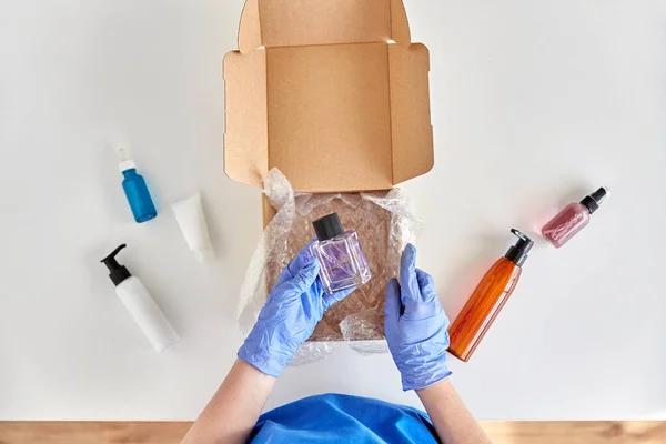 Händer i handskar förpackning paket låda med kosmetika — Stockfoto