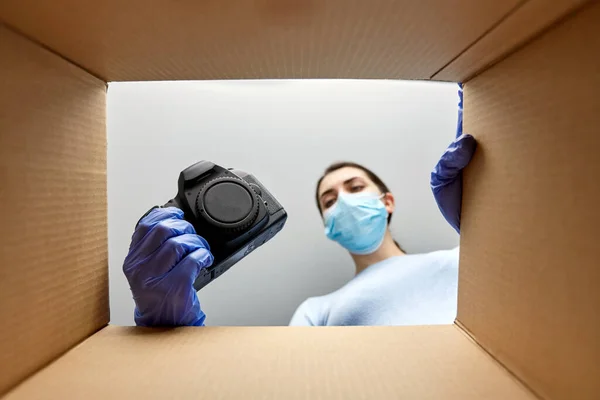 Kvinna i mask packning kamera i paket låda — Stockfoto