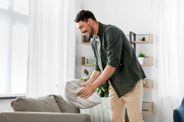 Feliz sorrindo homem organizando almofadas sofá em casa — Fotografia de Stock