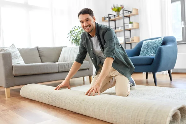 Feliz sonriente joven hombre desplegando alfombra en casa —  Fotos de Stock