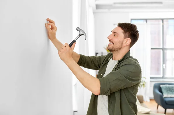 Sonriente hombre martillando clavo a pared en casa —  Fotos de Stock