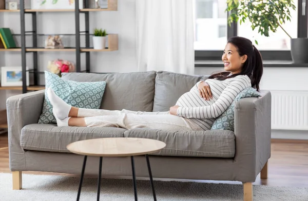 Heureux enceinte asiatique femme assis sur canapé à la maison — Photo