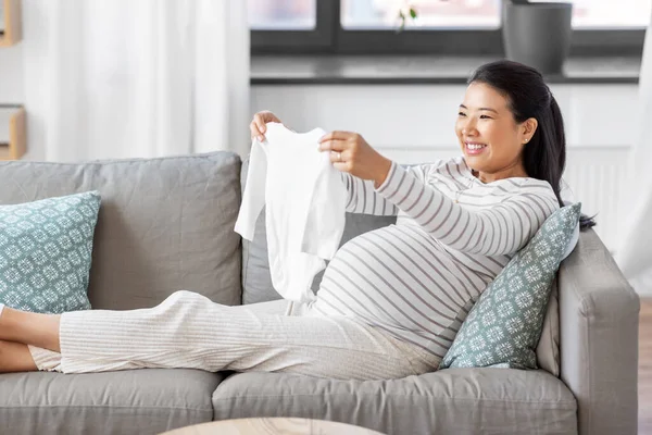 Gelukkig zwanger vrouw met babys bodysuit thuis — Stockfoto