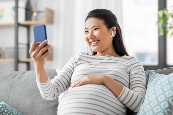 Zwangere vrouw met telefoon en oortjes thuis — Stockfoto