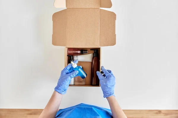 Hands in gloves packing parcel box with cosmetics — Stock Photo, Image