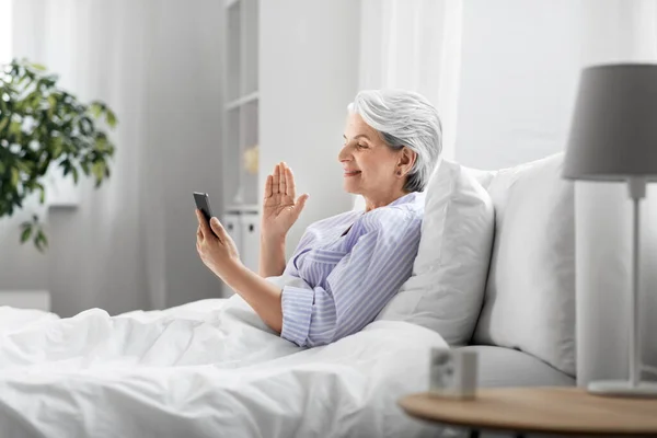 Senior woman with phone having video call in bed — Stock Photo, Image