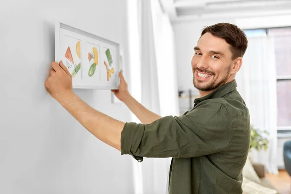 Hombre sonriente decorando casa con la imagen en el marco — Foto de Stock