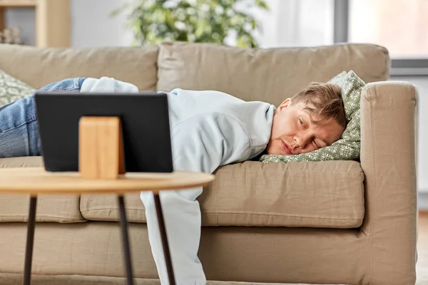 Hombre aburrido con la tableta PC acostado en el sofá en casa — Foto de Stock