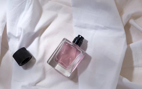 Lahvička parfému a uzávěr na bílém prostěradle — Stock fotografie